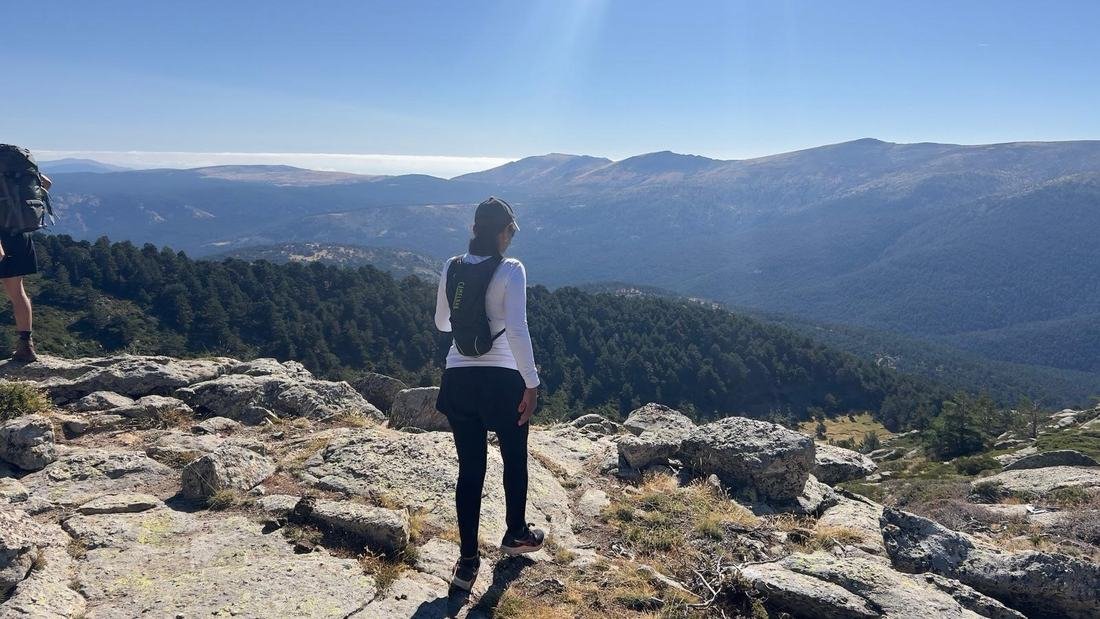 Yugliss Crespo de espaldas, observando un valle de montaña desde un mirador rocoso.